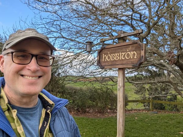 The bespeckled author standing in front of the town sign of Hobbiton
