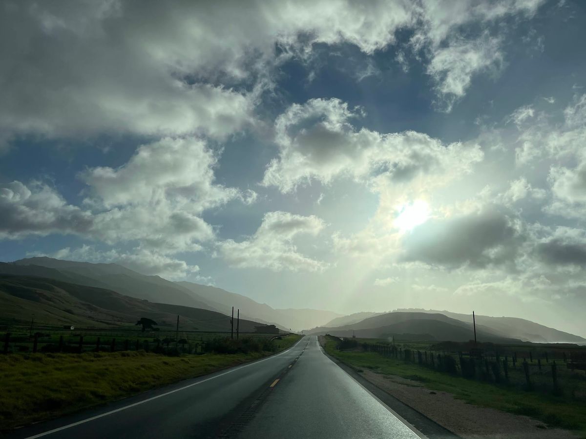 A road running toward a burst of light under big clouds