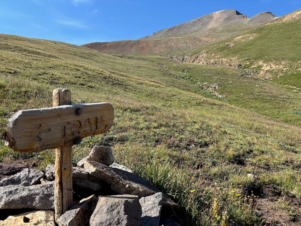 Wooden sign that says trail, with a big peak in the back