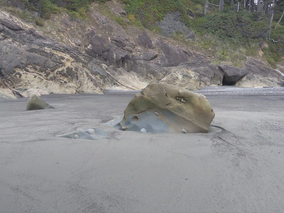 A big rock on a beach with other rocks in it.