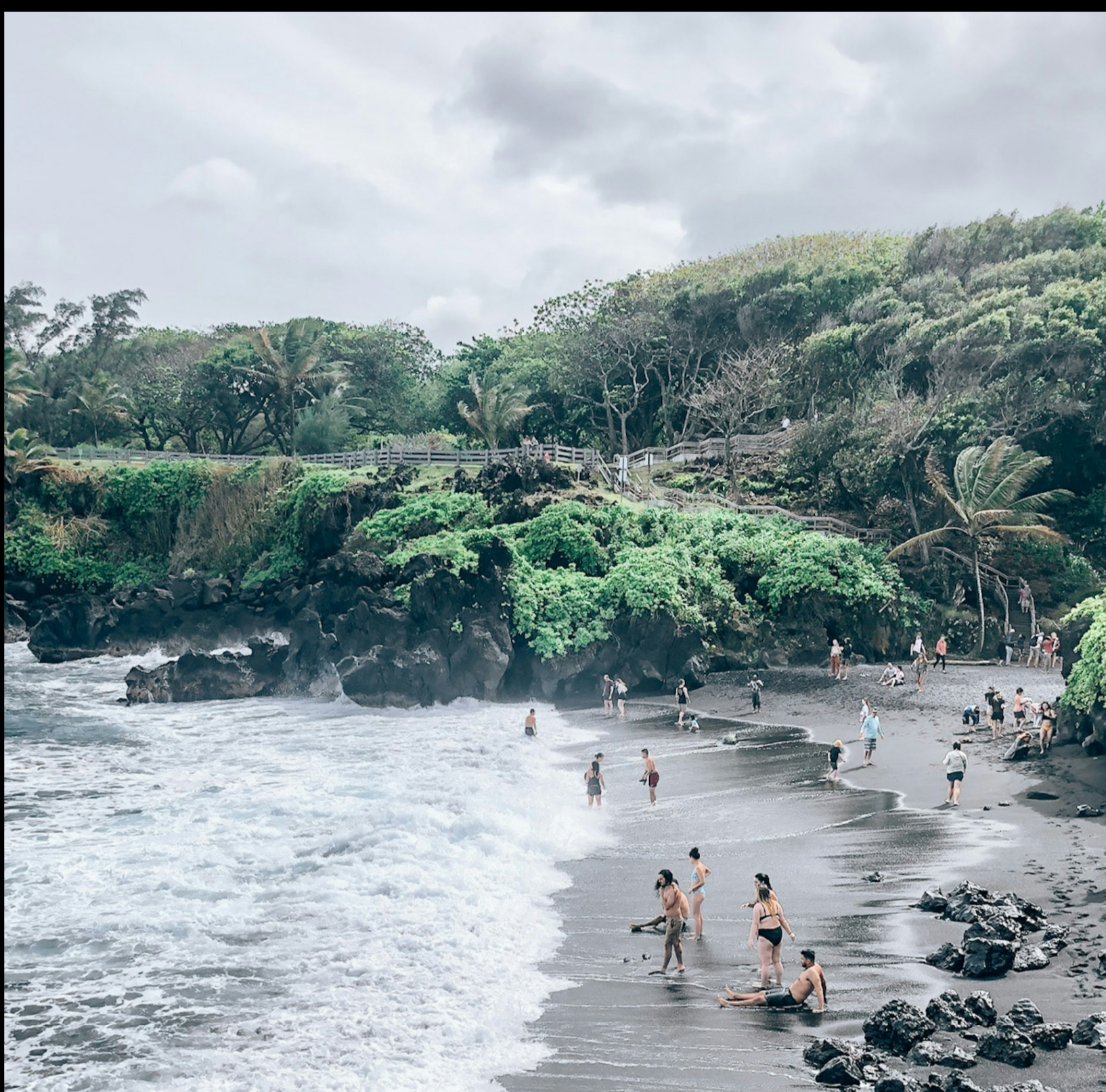 Travellers on a black-sand beach cove in Maui, Hawaii, USA