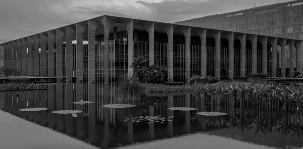 Fotografia em preto e branco do Palácio do Itamaraty em Brasília, refletido na água.
