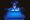 A laboratory researcher wearing protective gloves and a face shield carefully handles a gel electrophoresis tray under blue UV illumination.
