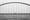 Cyclist crossing a long arched bridge over water in fog, black and white.