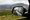 A car's side mirror reflecting the road behind, with misty mountains beyond.