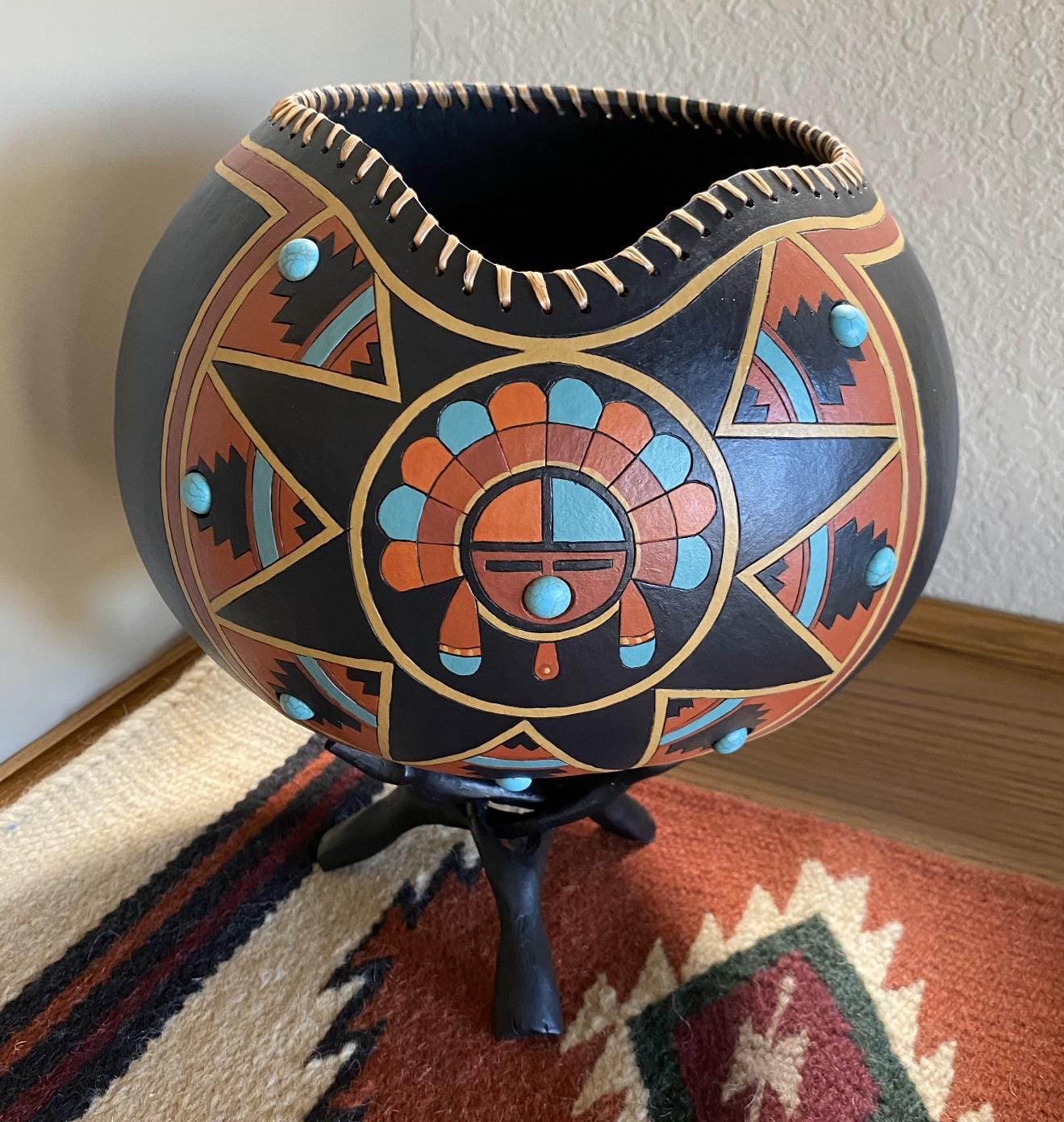 Decorated gourd with geometric patterns in red, turquoise and black on a wooden stand.