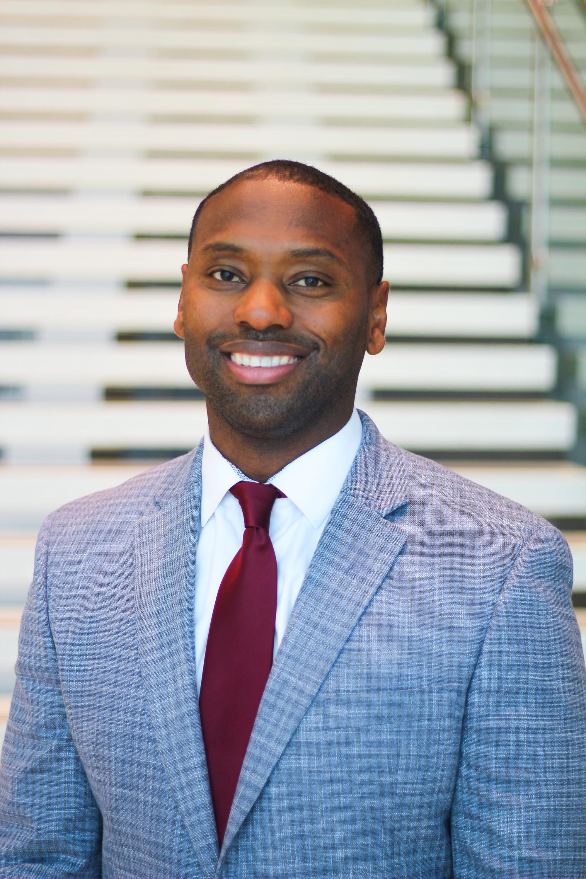 Joe Fields, New Mexico State University’s newly named athletics director, smiles while wearing a light gray suit and red tie in front of blurred steps