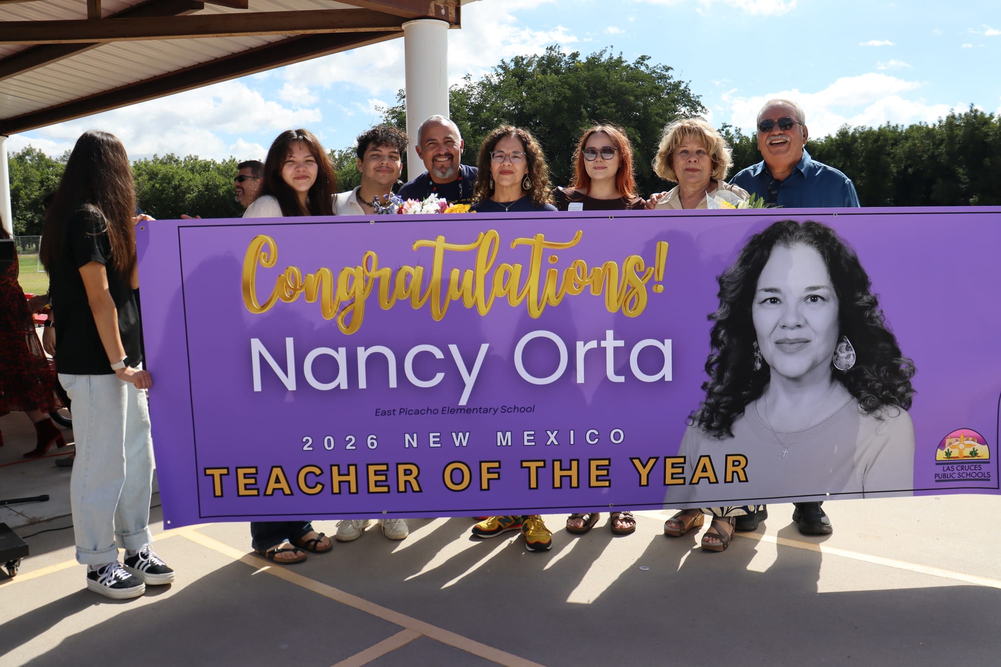 Nancy Orta stands with her family behind a banner celebrating her as the 2026 New Mexico Teacher of the Year at East Picacho Elementary in Las Cruces.