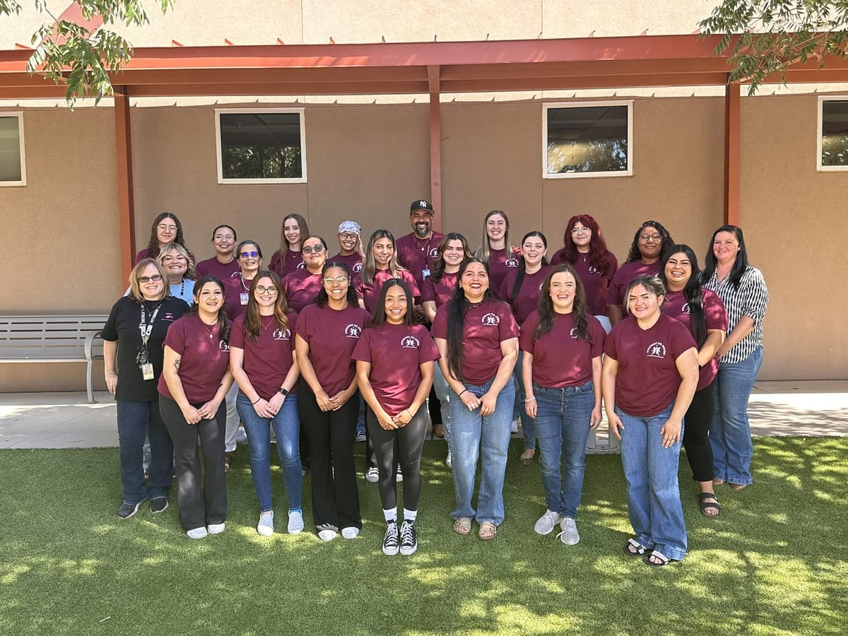 Group photo of NMSU social work students and Las Cruces Public Schools staff standing outside, many wearing matching maroon shirts.