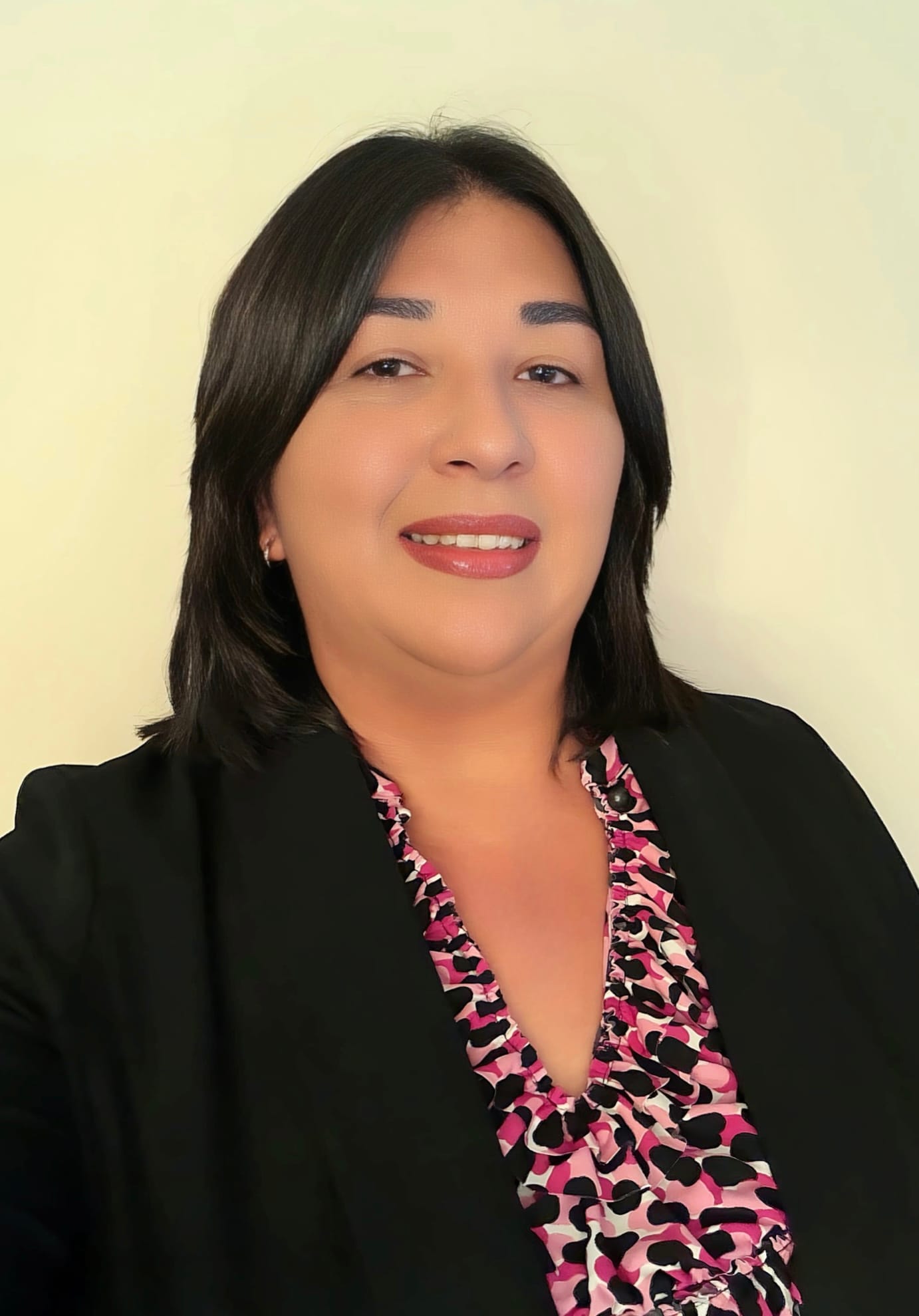 Denisse Carter, newly appointed Economic Development Director for Doña Ana County, wearing a black blazer and patterned pink blouse against a light background.
