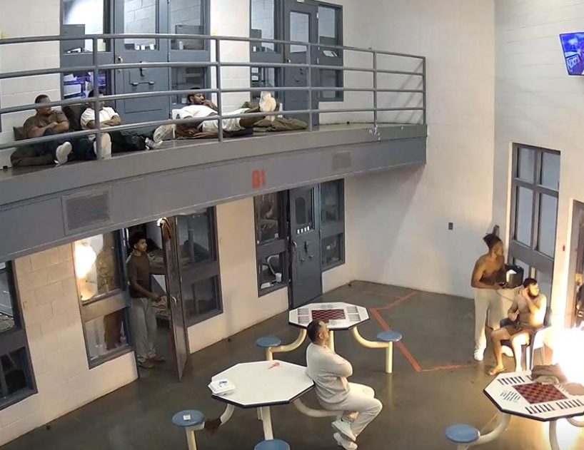 Surveillance footage shows detainees inside a two-tier housing unit at the Doña Ana County Detention Center, with several men sitting or lying on bunks and tables while others stand near cell doors.