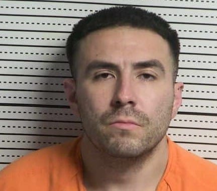 Mugshot of a man wearing an orange jail uniform standing against a height-marked wall.