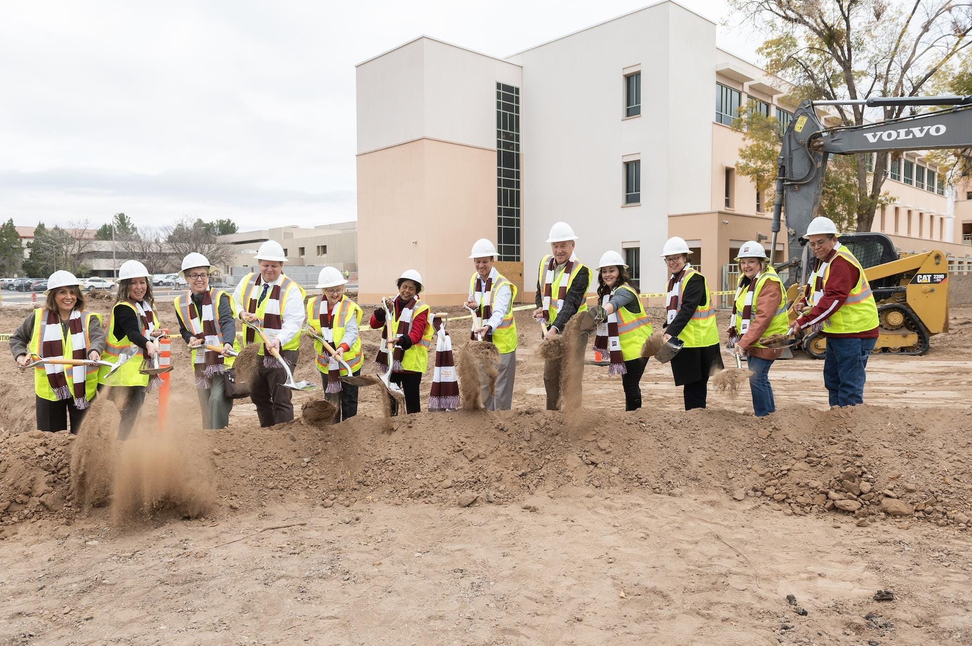 People using shovels to dig through a mound of dirt outside of a building.