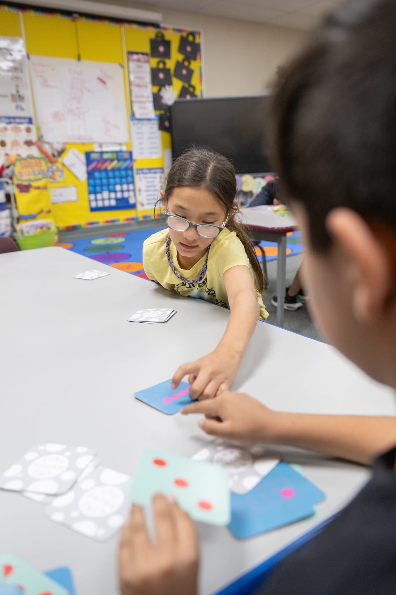A young student reaches across a classroom table to match colorful math cards during an NMSU STEM Outreach Center learning activity.