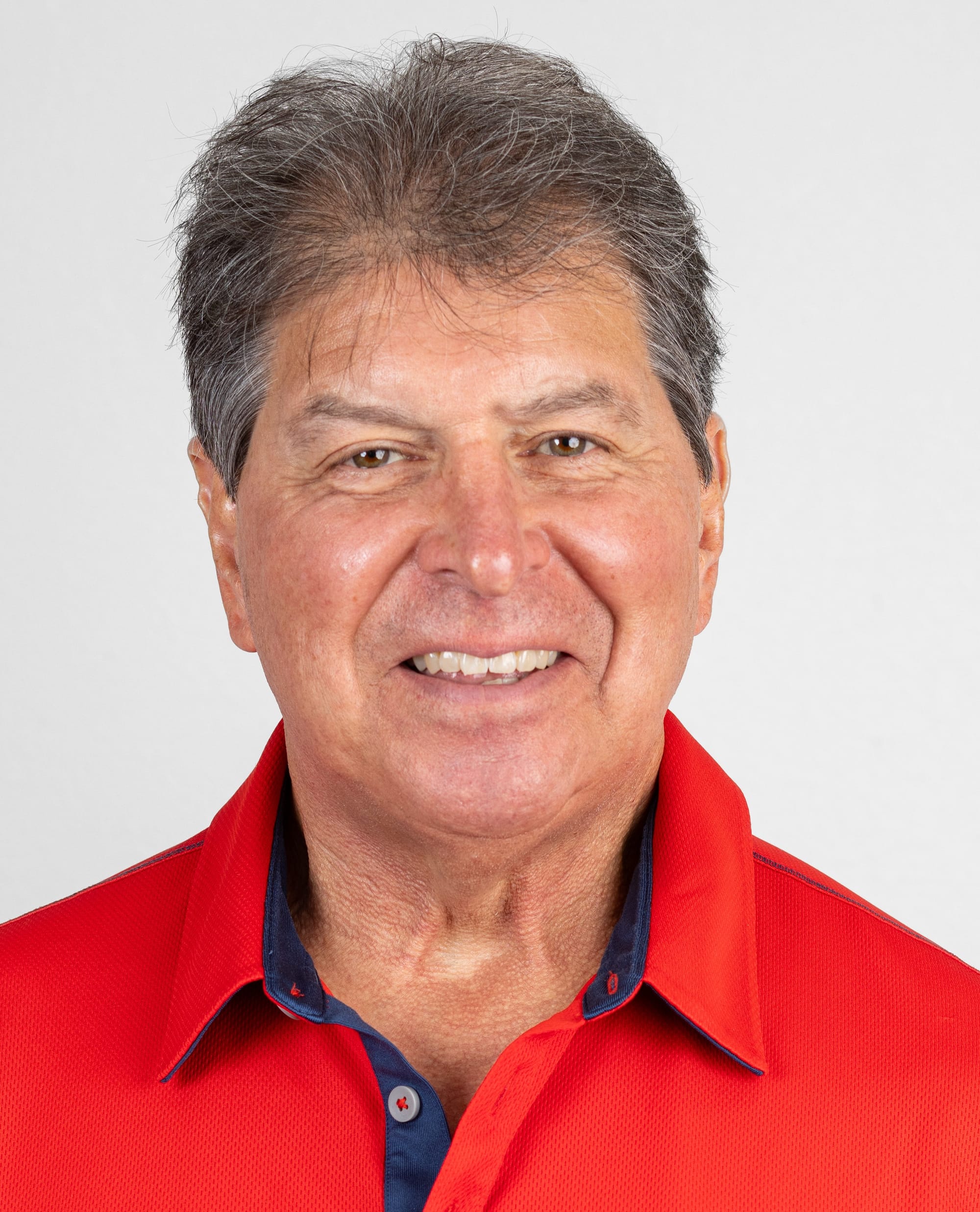 Portrait of John Cordova smiling at the camera, wearing a red collared shirt against a light, neutral background.