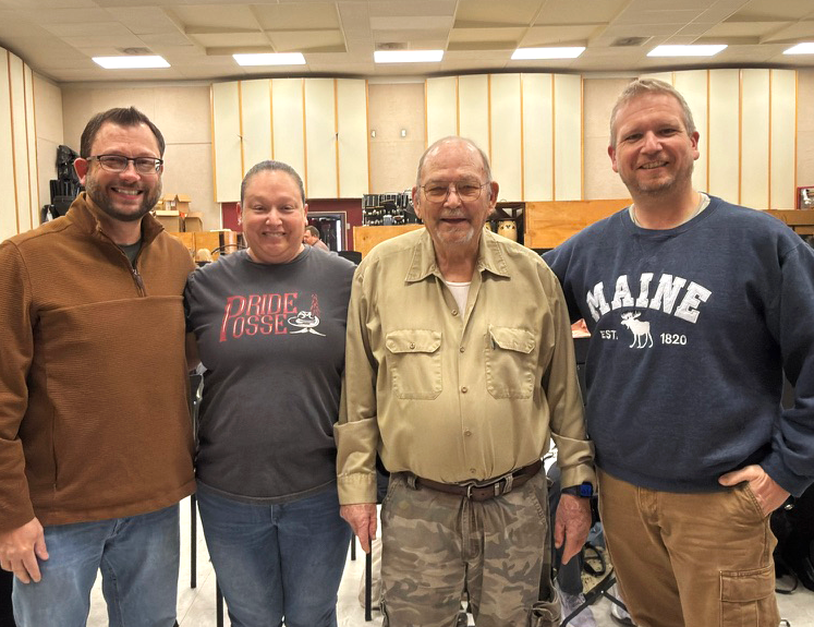 Rod Pior, Karen Padilla, Jim Young and Dr. Michael Mapp stand together in the NMSU band room, smiling in front of music stands and percussion instruments.