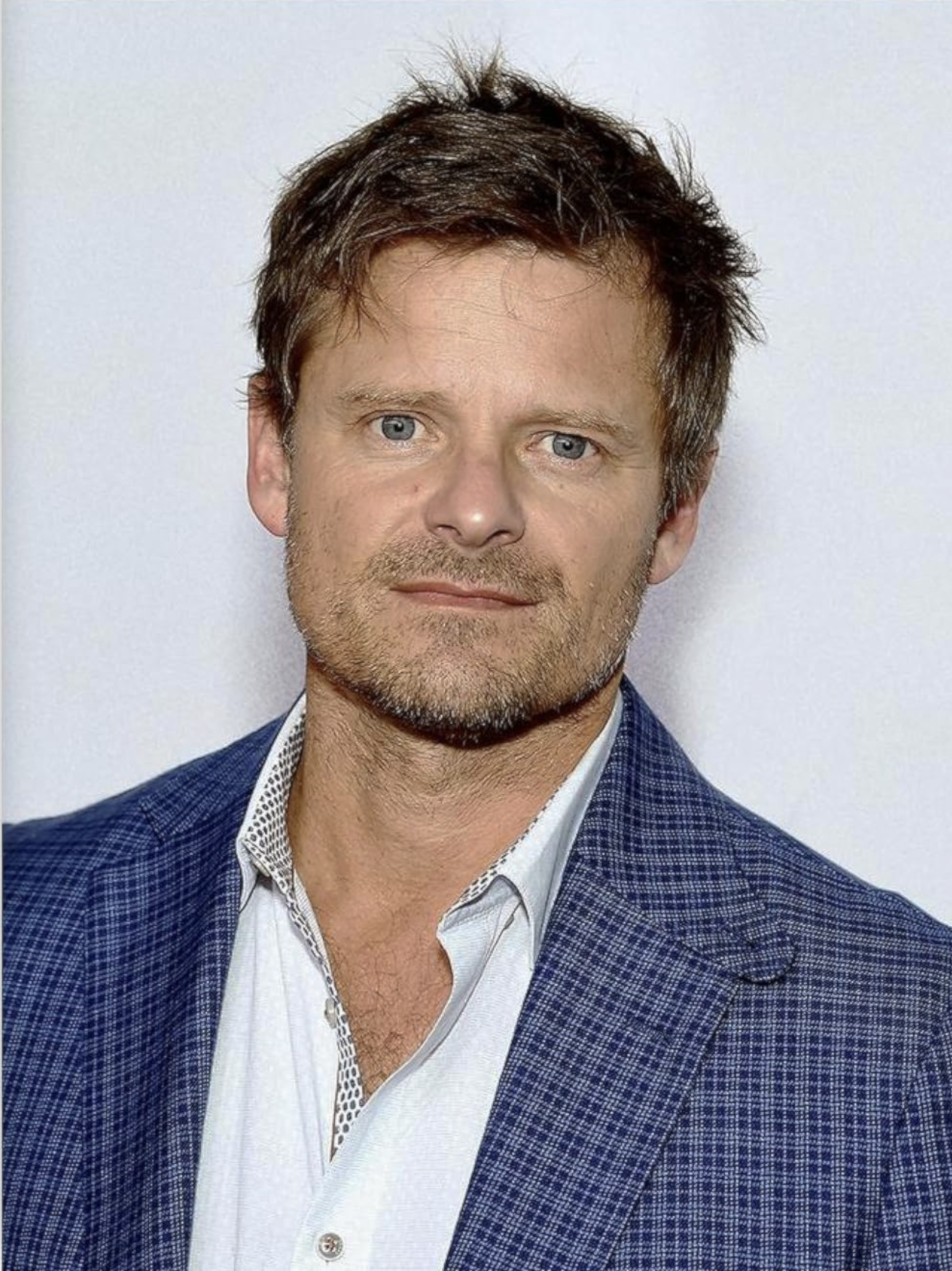 Actor Steve Zahn poses for a portrait wearing a blue jacket and light shirt against a plain background.