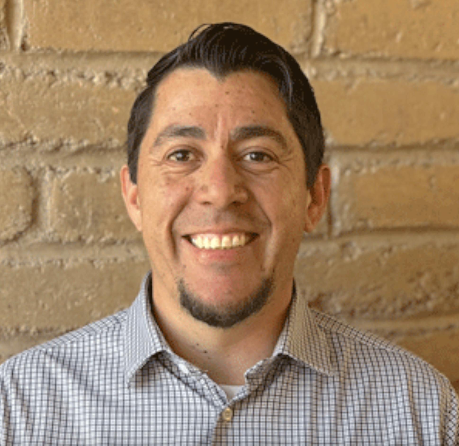 Mesilla Mayor Russell Hernandez smiles in a headshot portrait against a brick wall background.