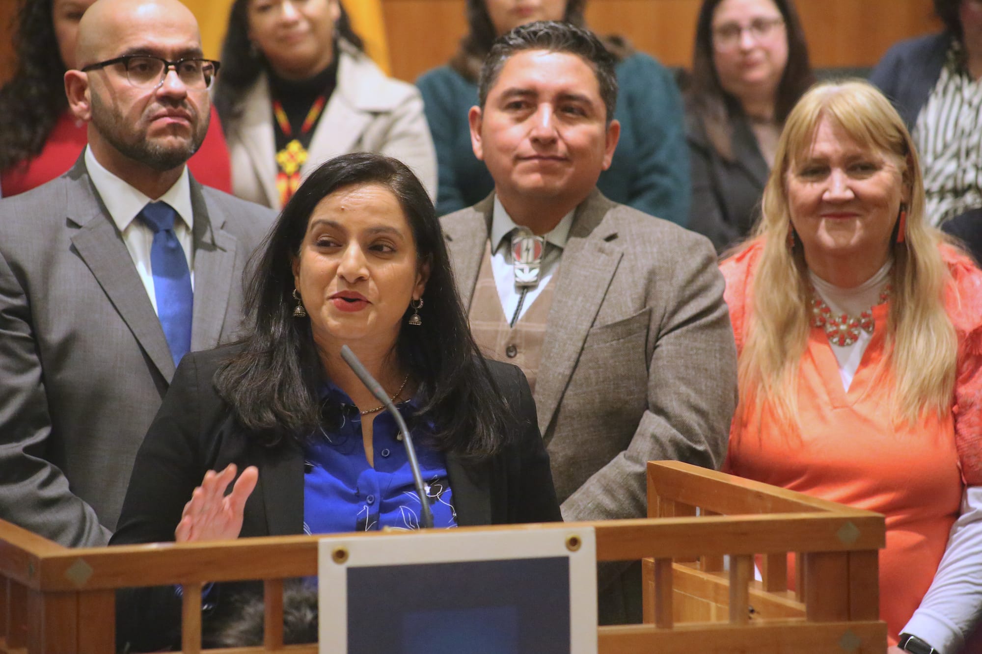 Rep. Reena Szczepanski speaks at a podium on the House floor during a Feb. 19 news conference following the end of the legislative session, with Democratic lawmakers standing behind her.
