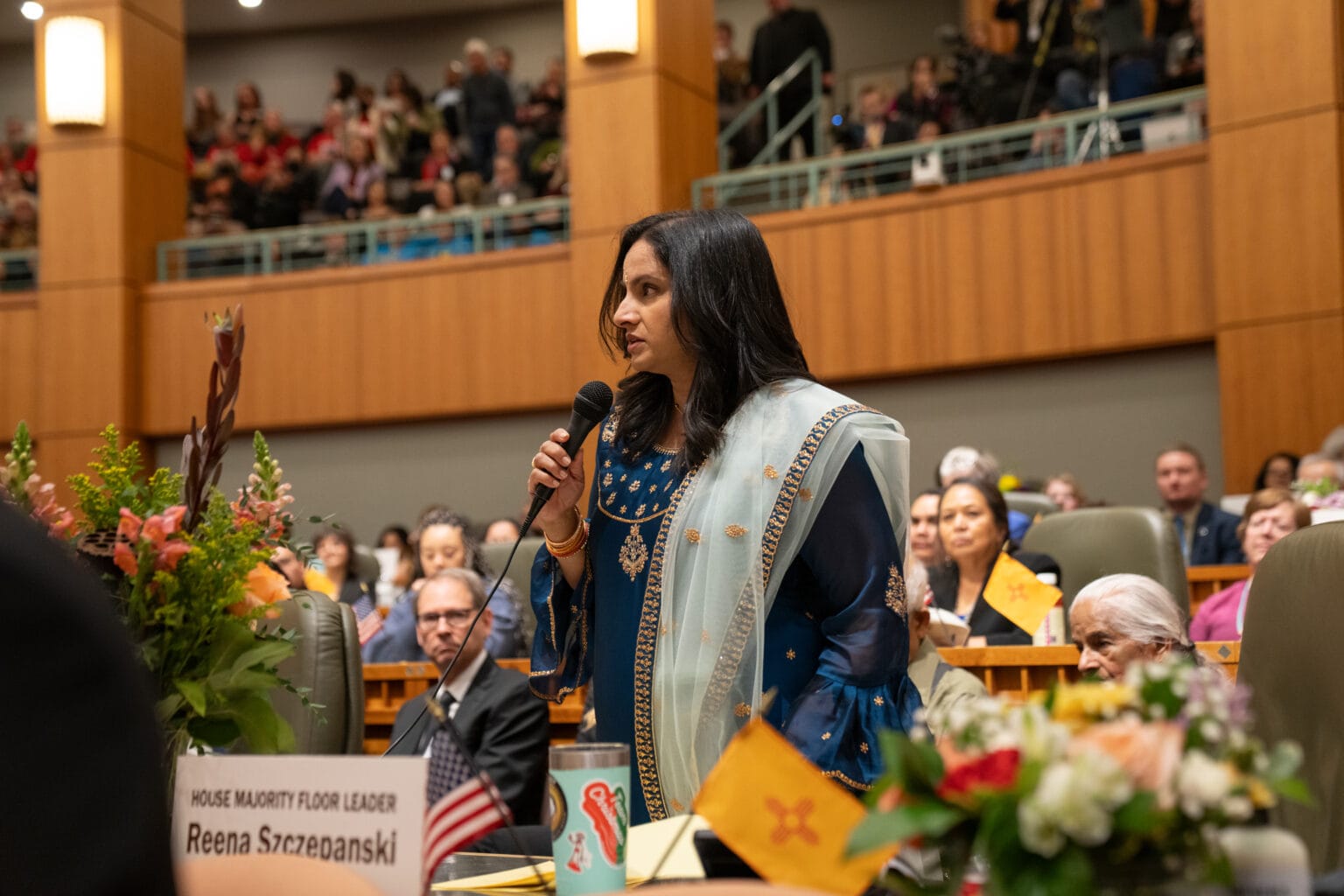 New Mexico Rep. Reena Szczepanski speaks on the House floor at the Roundhouse while holding a microphone during a legislative session.
