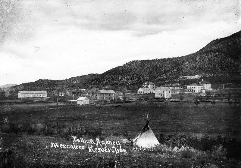 Historic view of the Mescalero Apache Reservation showing buildings and a tipi in the foreground.