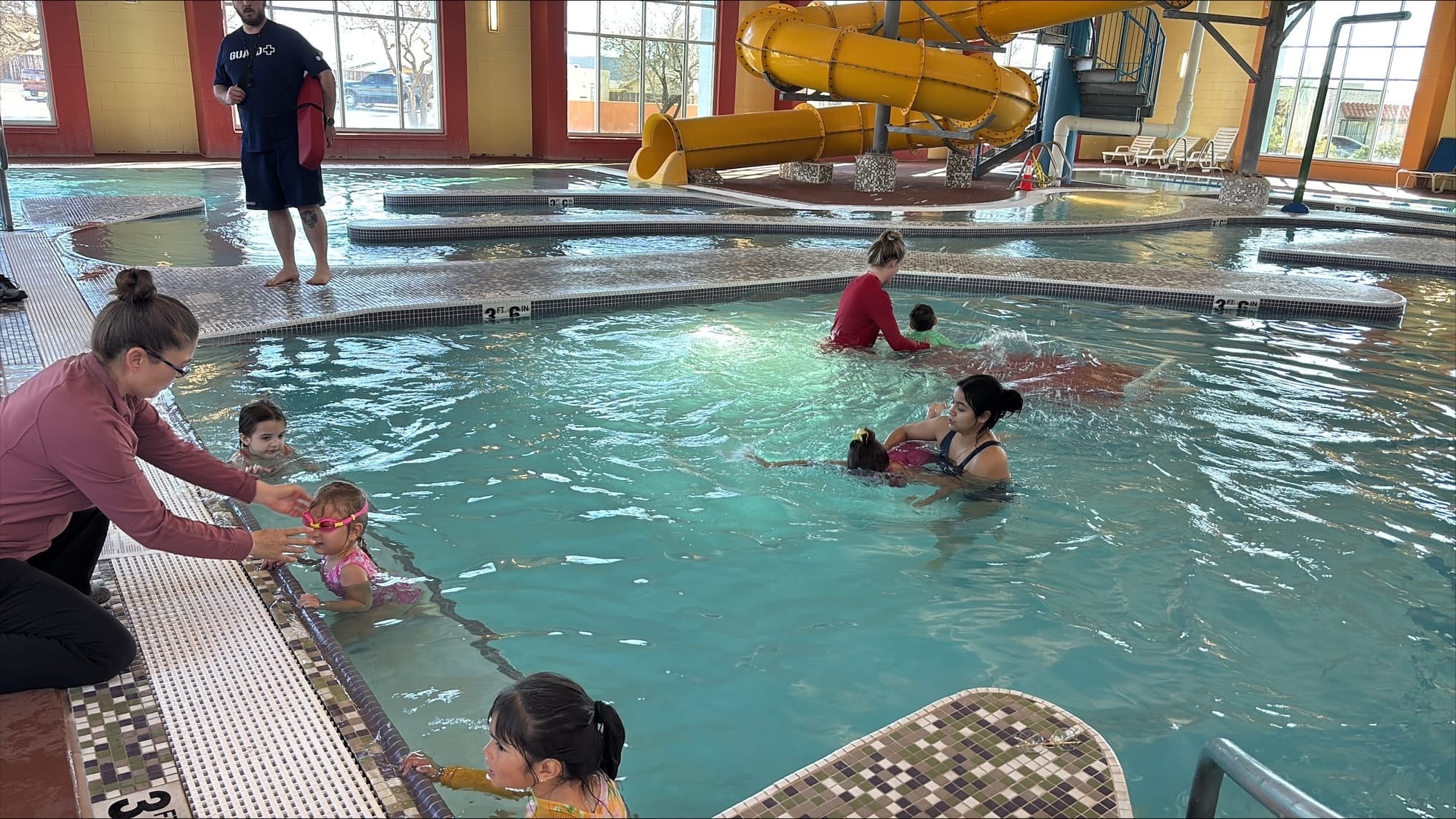 Parents and children participate in a swim lesson at an indoor pool at a Las Cruces aquatic facility.