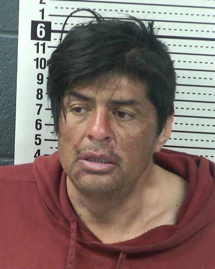 Booking photo of Manuel Saenz wearing a red hoodie in front of a height chart at the Doña Ana County Detention Center.