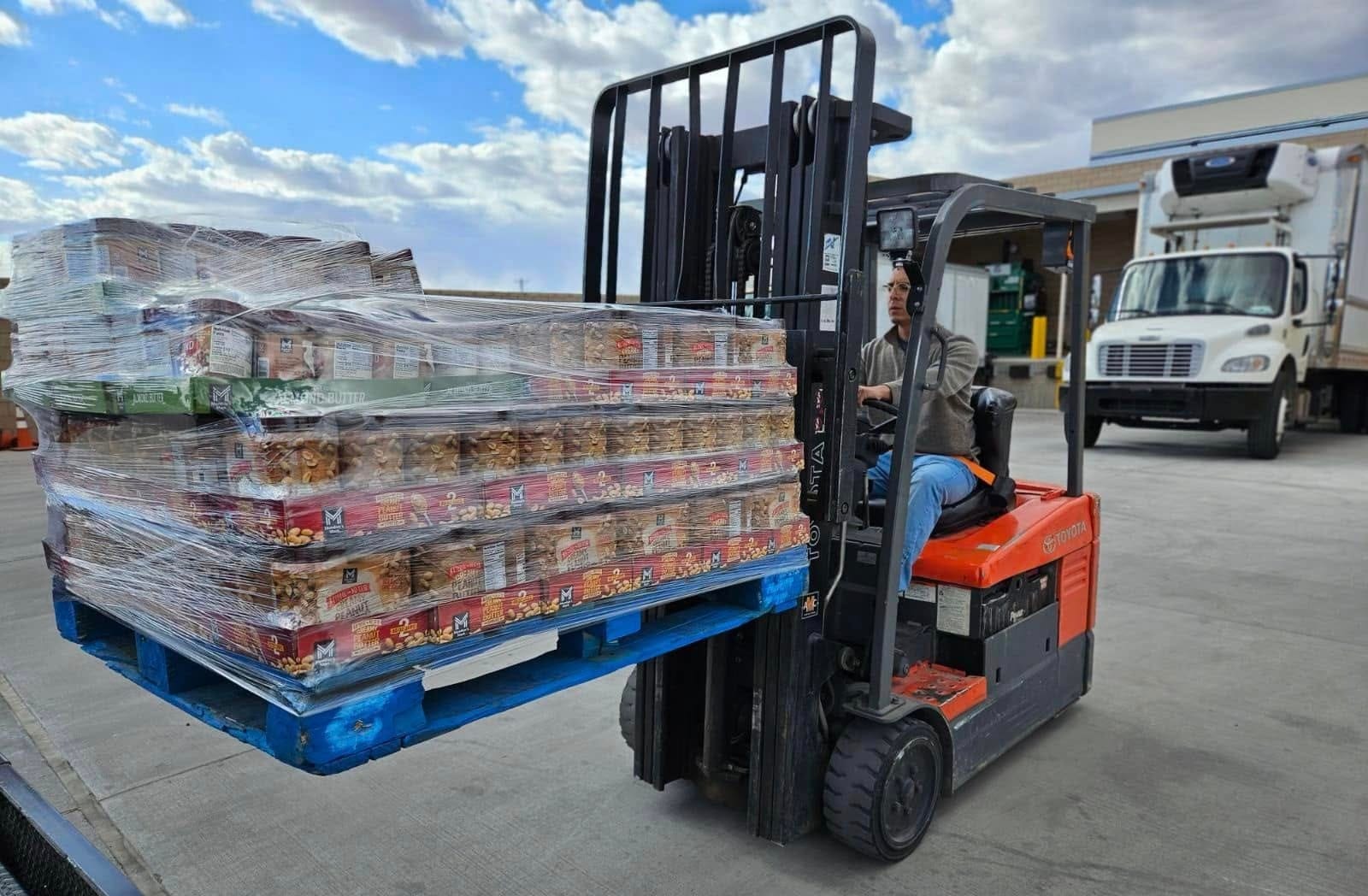 A forklift operator moves a pallet of packaged peanut butter at a food distribution facility.