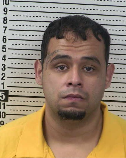 Mugshot of Adrian J. Mora wearing a prison-issued yellow shirt in front of a height chart