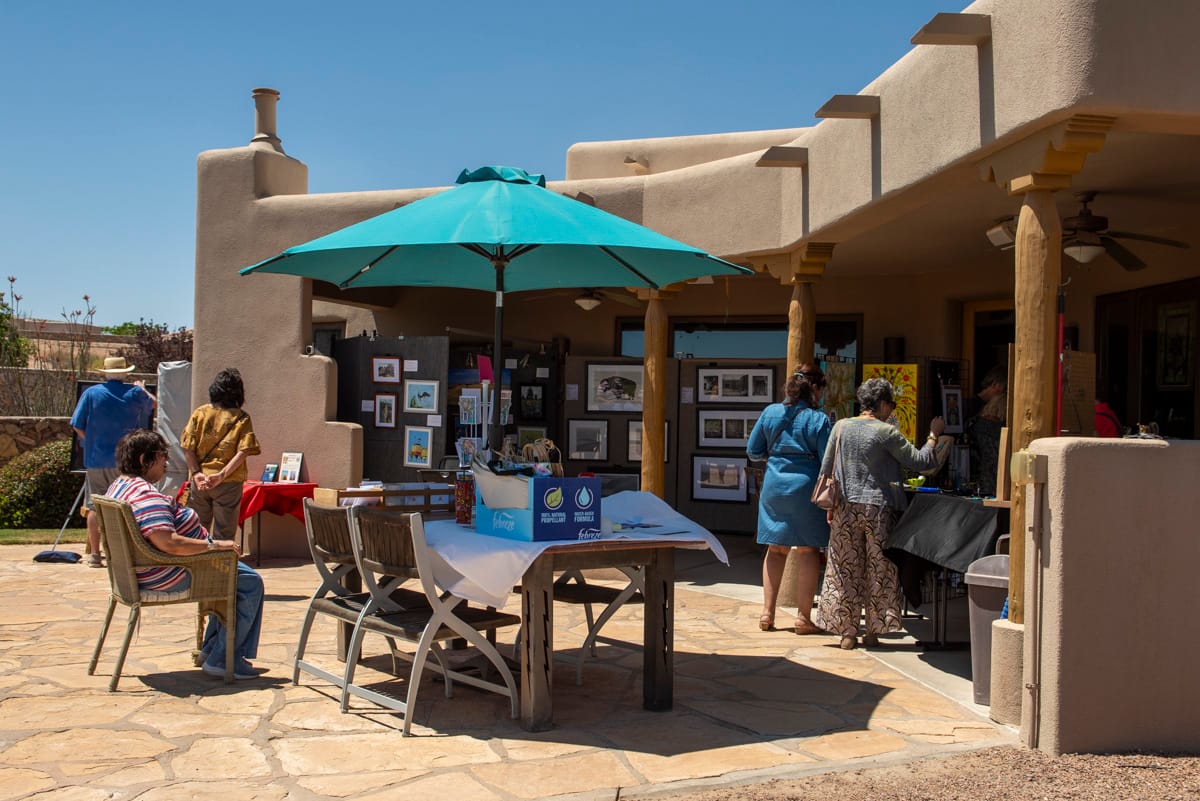 People viewing artwork displayed on patio walls and tables during an outdoor garden art show.