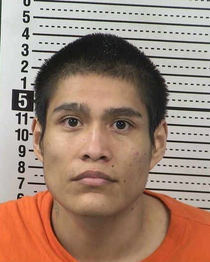 Booking photo of Dominic James Isaac Sandoval Peralta wearing an orange shirt, facing forward with a neutral expression in front of a height chart.