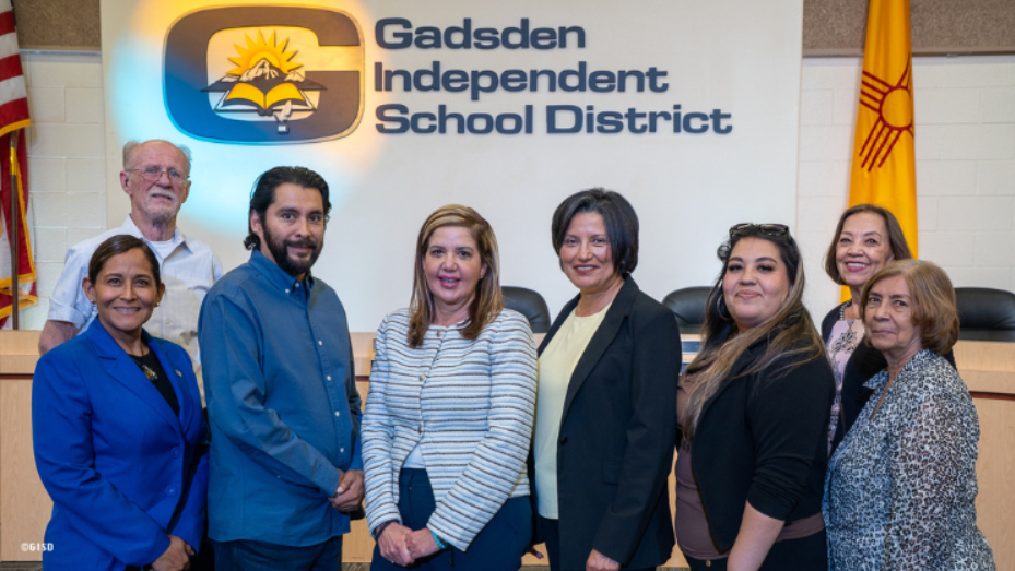 Nubia Tarazona stands with members of the Gadsden Independent School District Board of Education and search facilitators in front of the district logo