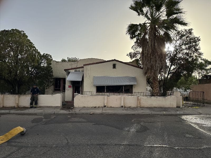 Front view of an abandoned building on North Mesquite Street in Las Cruces with a firefighter nearby and signs of recent fire damage.