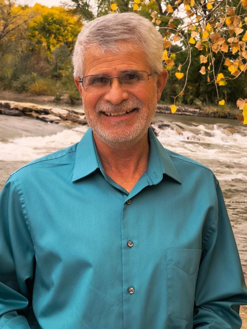 Matt Dodson stands outdoors near a river, wearing a teal shirt, in a campaign-style photo.