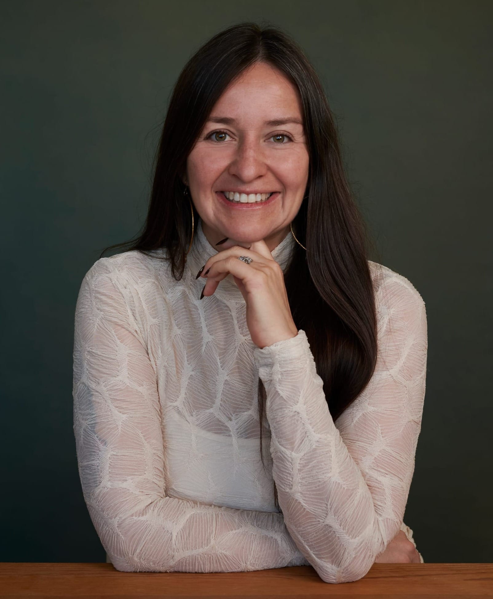 Micaela Lara Cadena poses for a studio portrait with her hand resting under her chin against a neutral background.