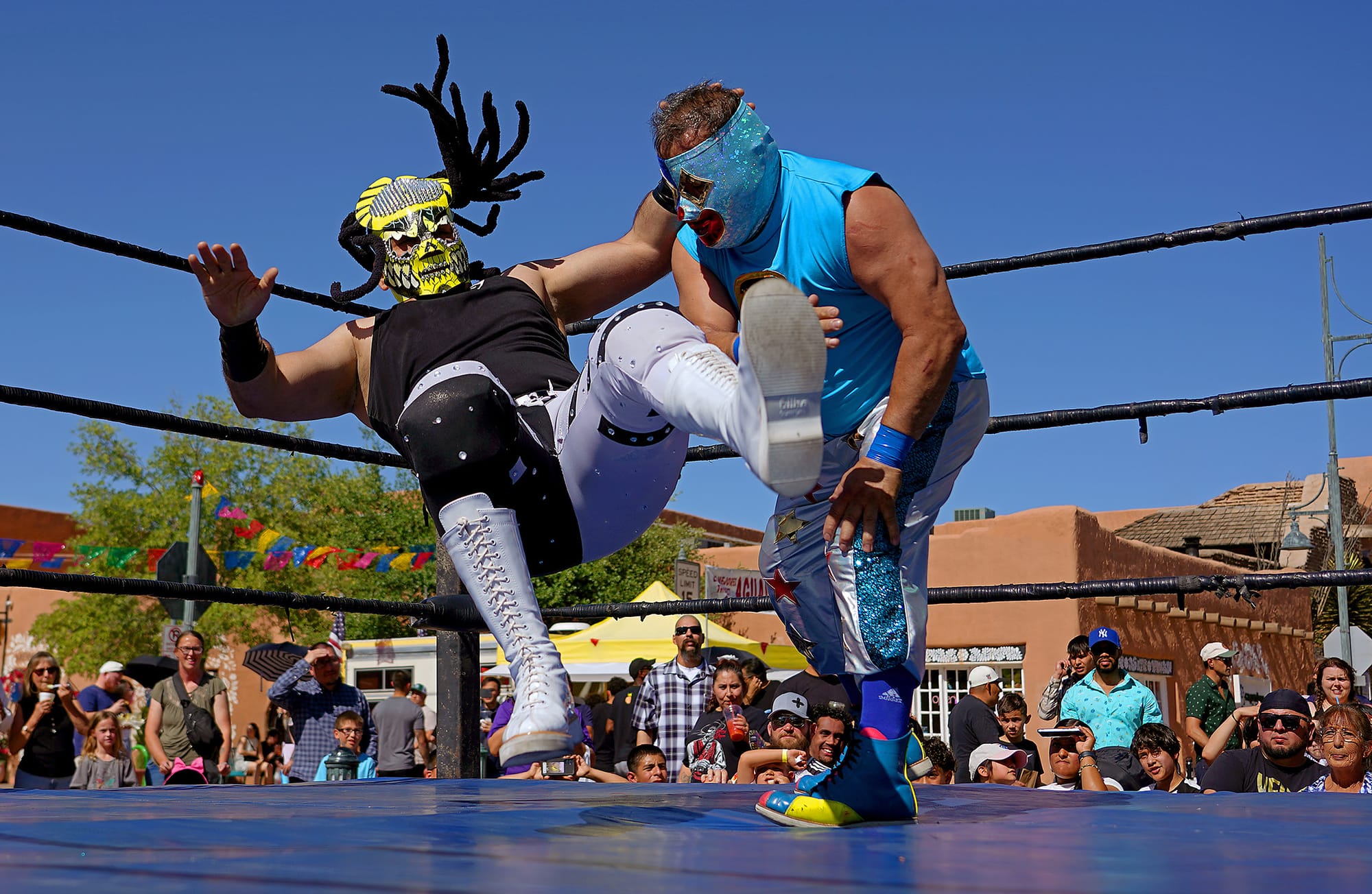 Two masked lucha libre wrestlers perform in an outdoor ring as a crowd watches during a festival in downtown Las Cruces.