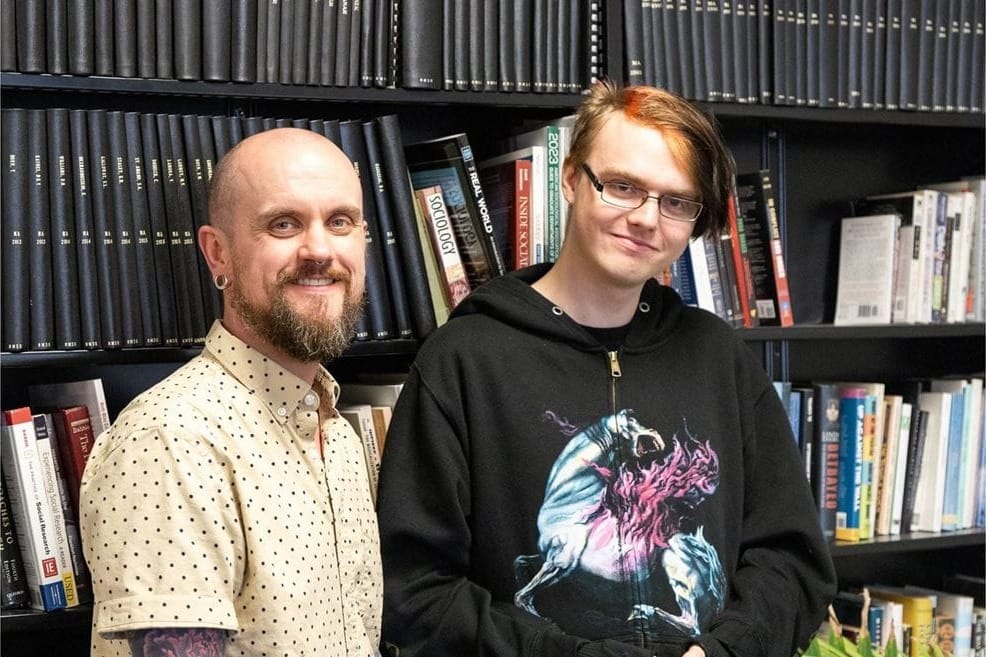 Cade Borner, an NMSU sociology senior, stands with mentor Marshall Taylor, a sociology associate professor, in front of bookshelves while working on a Discovery Scholars research project.