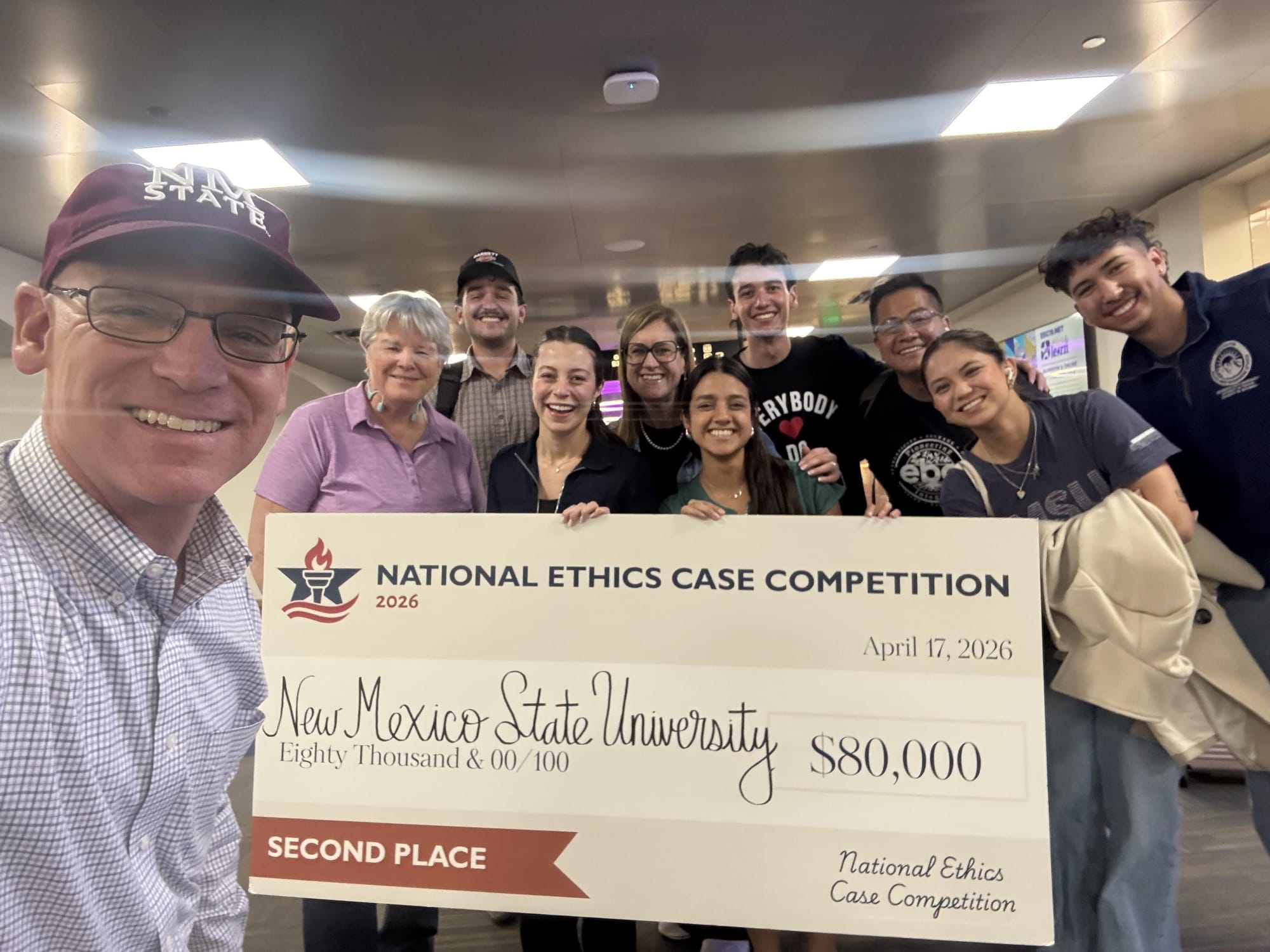 NMSU students and faculty smile and hold a large $80,000 check after placing second at a national ethics case competition.