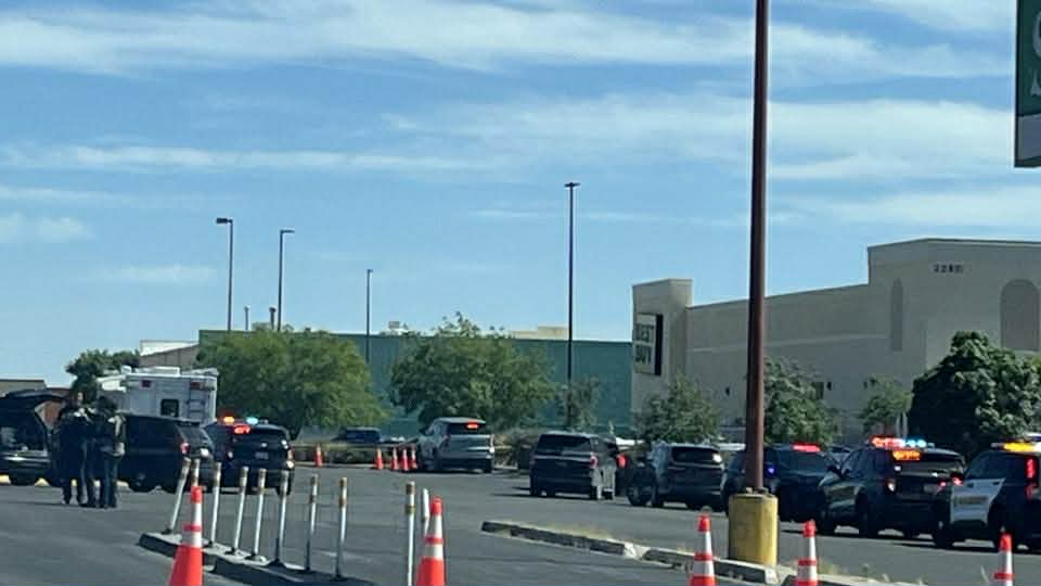 Multiple police vehicles and emergency responders are positioned in a parking lot near east Lohman Avenue, with traffic cones set up around the scene.