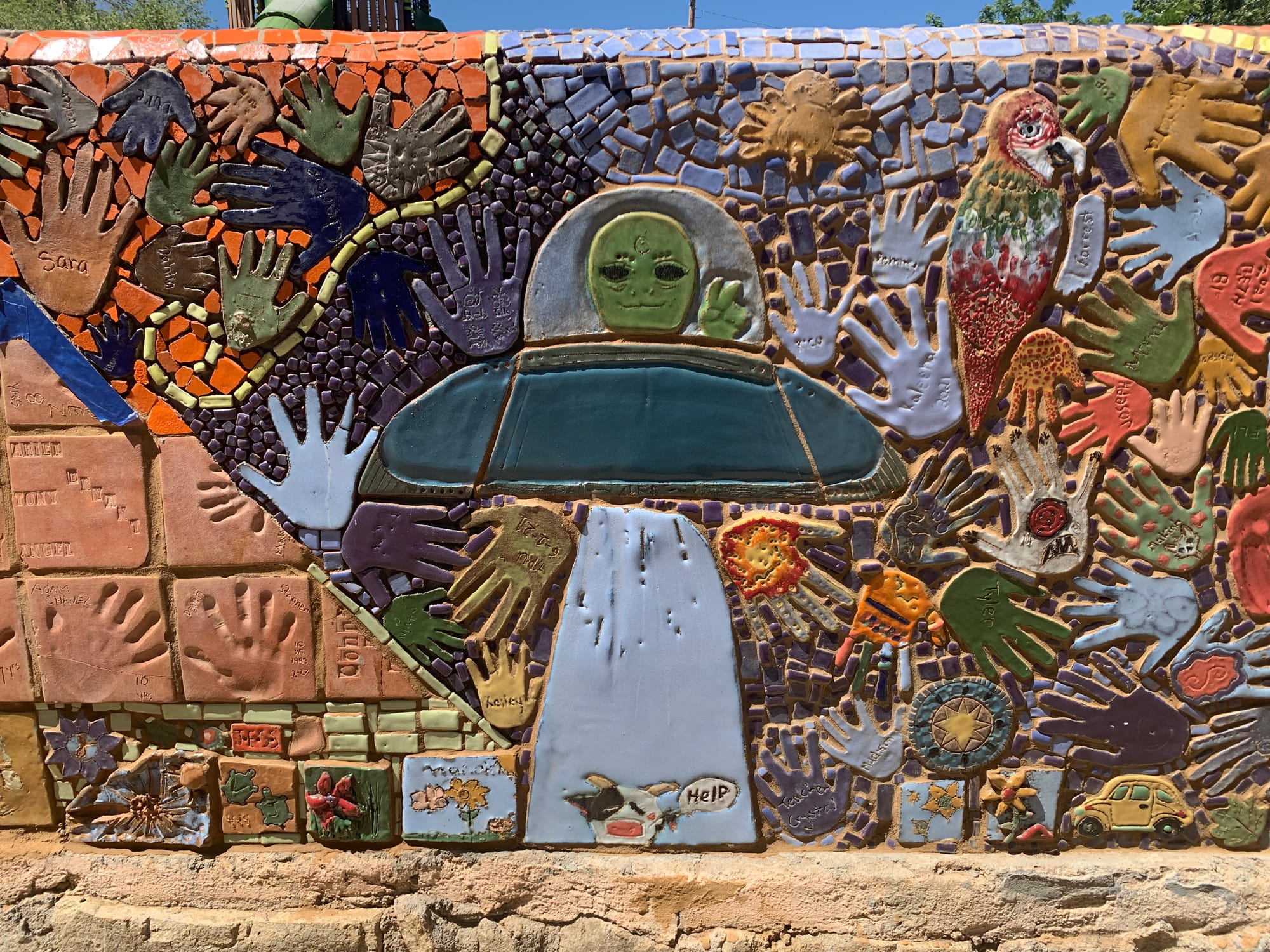 Colorful mosaic mural in Silver City’s Penny Park created by the Youth Mural Program, featuring handprints, animals and a central alien figure.