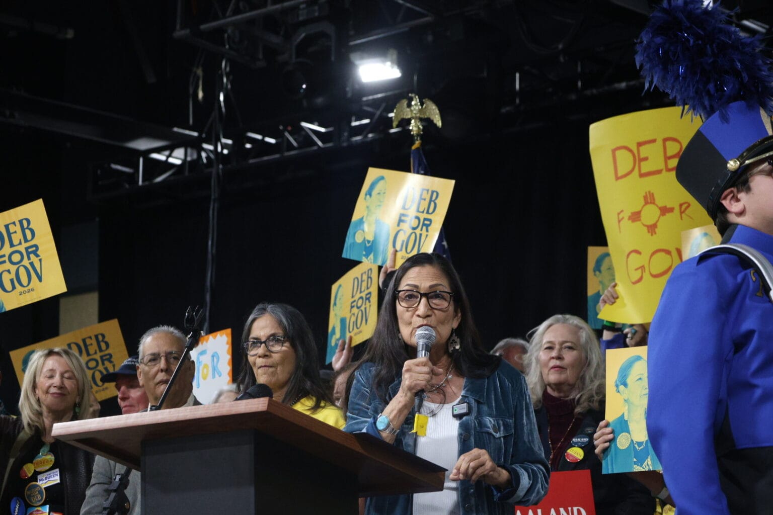 Deb Haaland speaks at a campaign event while supporters hold “Deb for Gov” signs in the background.