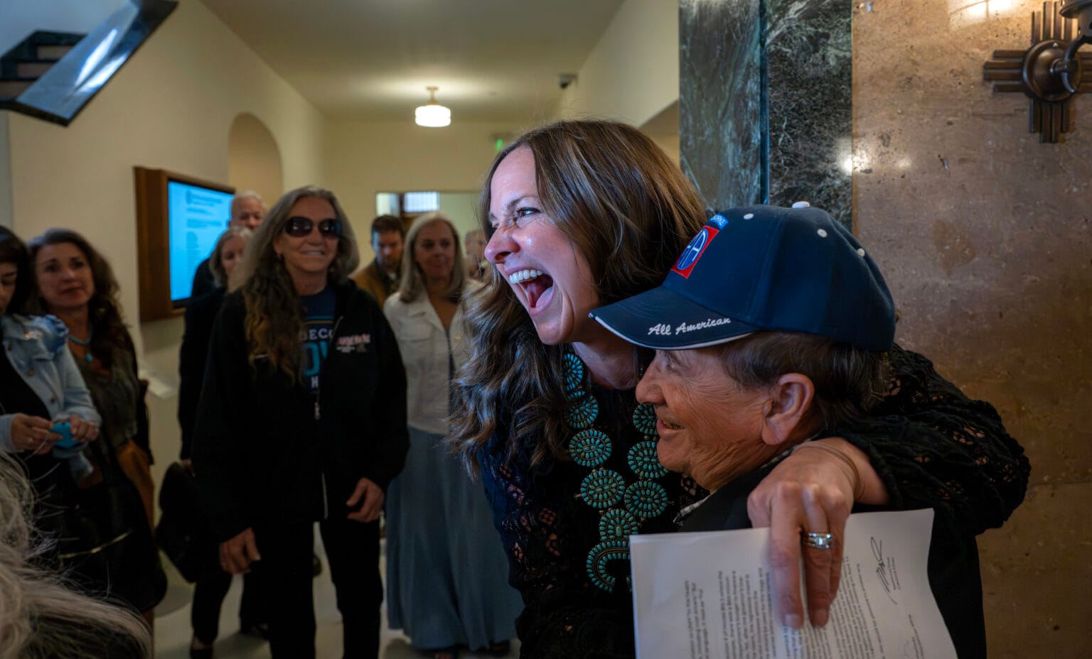 Rep. Rebecca Dow smiles and hugs a supporter inside a government building after a court decision, surrounded by onlookers.