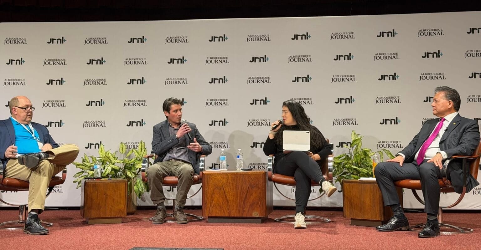 Ken Miyagishima sits on a panel at an Albuquerque Journal town hall, speaking alongside moderators onstage.