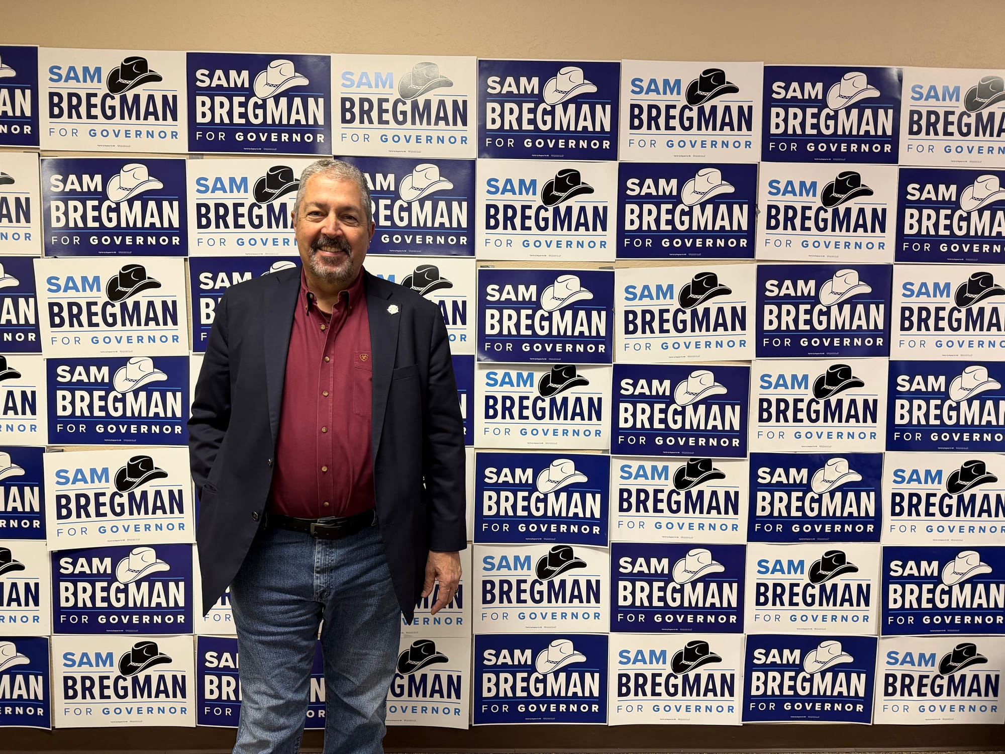 Sam Bregman stands in front of a wall of “Sam Bregman for Governor” campaign signs.
