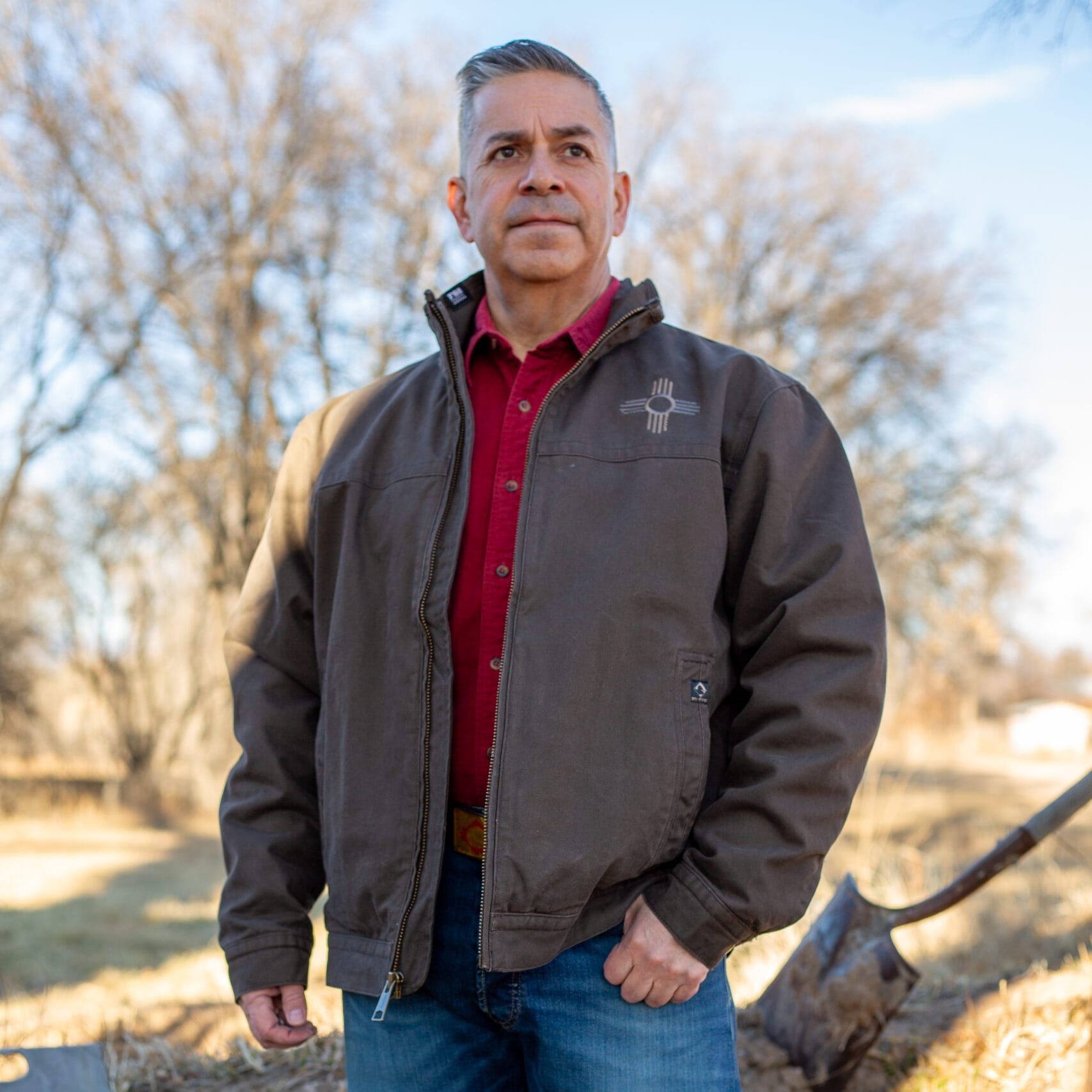 U.S. Sen. Ben Ray Luján stands outdoors wearing a jacket over a red shirt in a campaign-style photo.