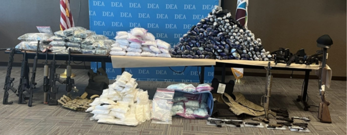 Table displaying seized cash, packaged drugs and multiple firearms during a federal investigation tied to the Syndicato de Nuevo Mexico gang.