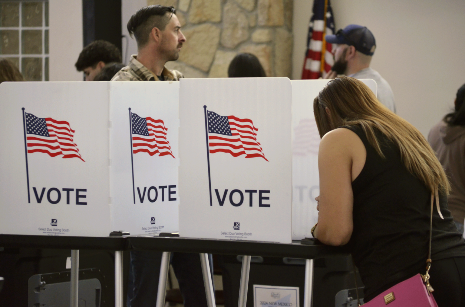 A voter fills out a ballot at a voting booth with American flags during a New Mexico election.