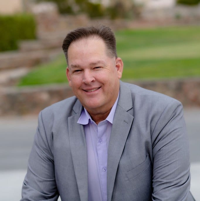 Republican Doña Ana County sheriff candidate Byron Hollister poses outdoors wearing a gray blazer and light purple shirt.