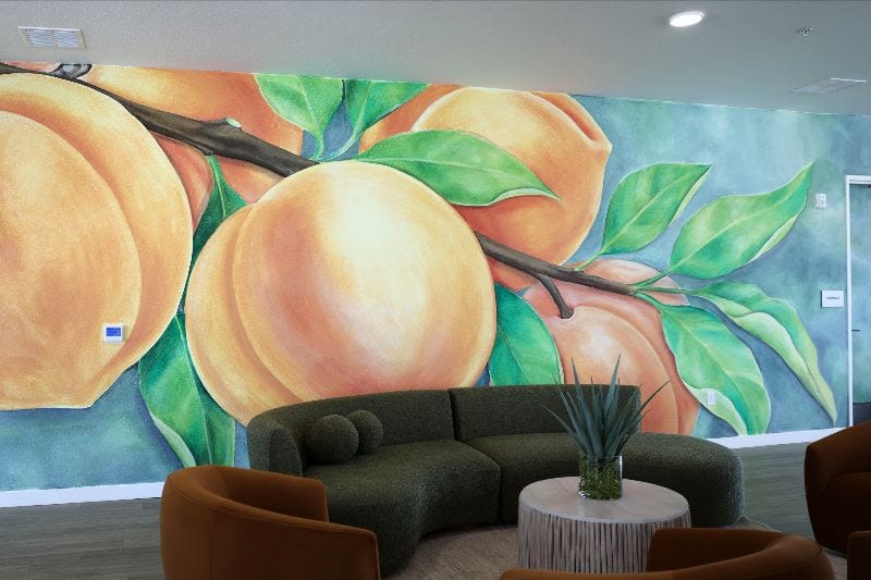 A colorful mural featuring peaches and green leaves covers a wall inside the Peachtree Canyon Apartments community space in Las Cruces.