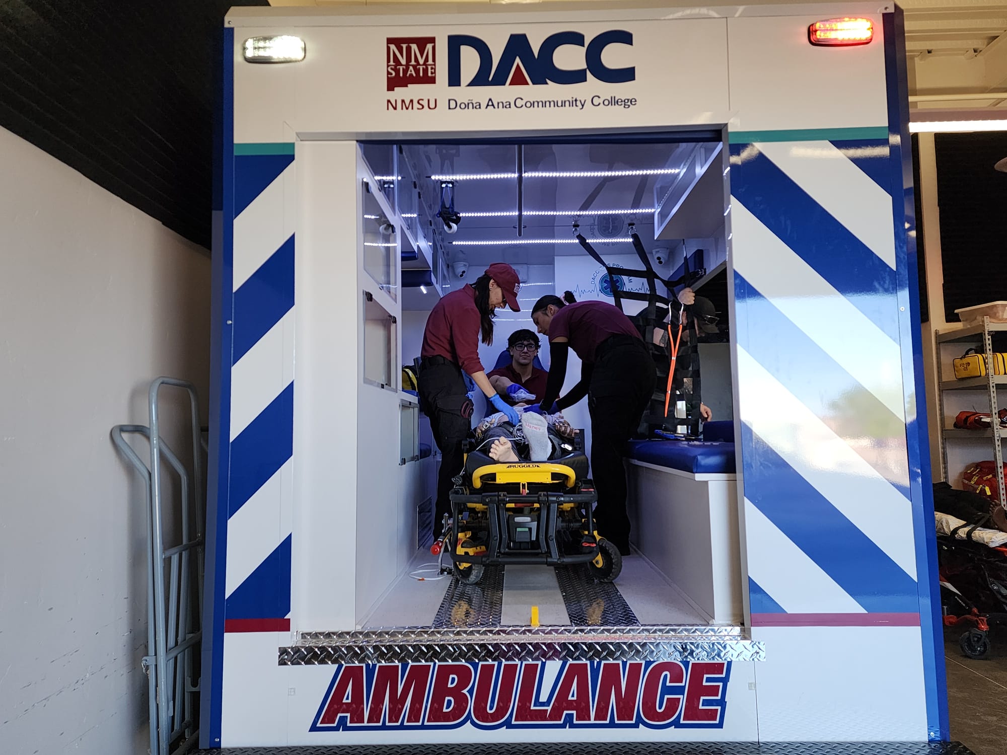 DACC EMS students work inside a training ambulance while assisting a patient on a stretcher during a hands-on classroom exercise.